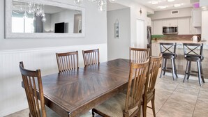 Un comedor con una mesa y sillas de madera, un espejo grande y lámparas colgantes.