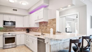 Una cocina moderna con gabinetes blancos, electrodomésticos de acero inoxidable, encimera de mármol y una isla integrada con taburetes de bar.
