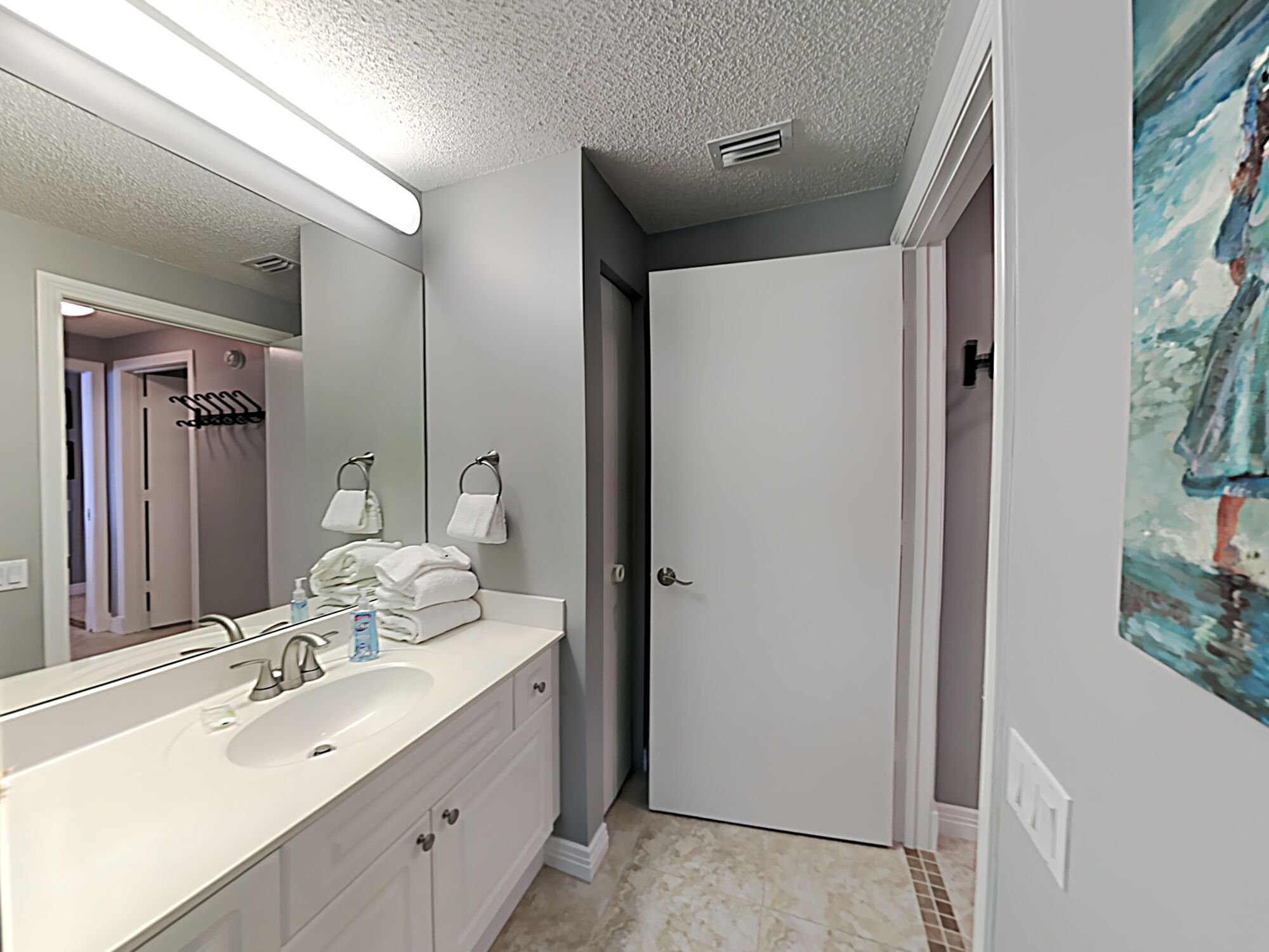 A bathroom with a white sink, mirror, and towel rack. There is a door leading to another room.