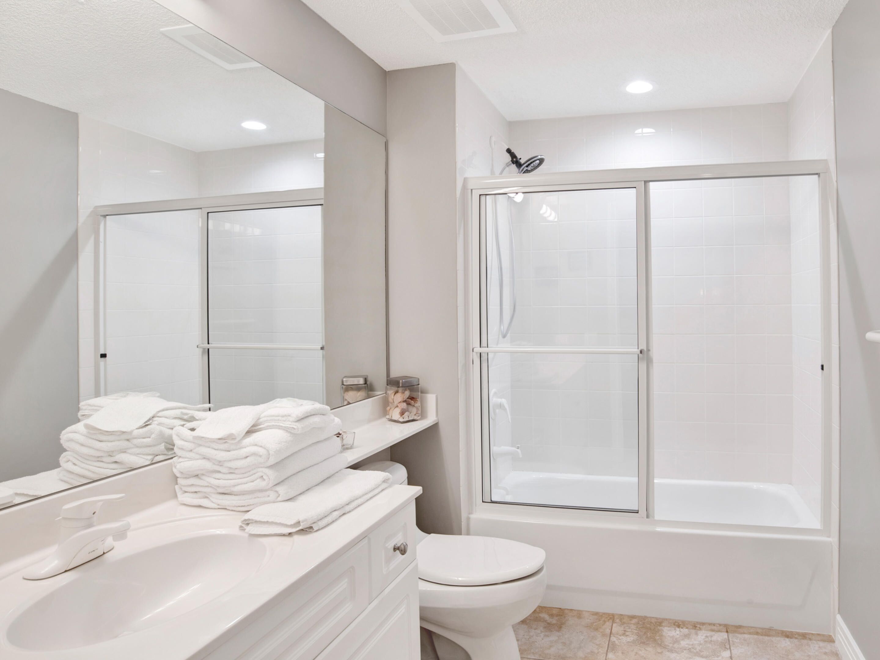 Une salle de bain moderne avec un meuble-lavabo blanc, des toilettes, une douche à parois de verre et un grand miroir.