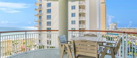 A balcony with a table and chairs, overlooking a beach and a cityscape.