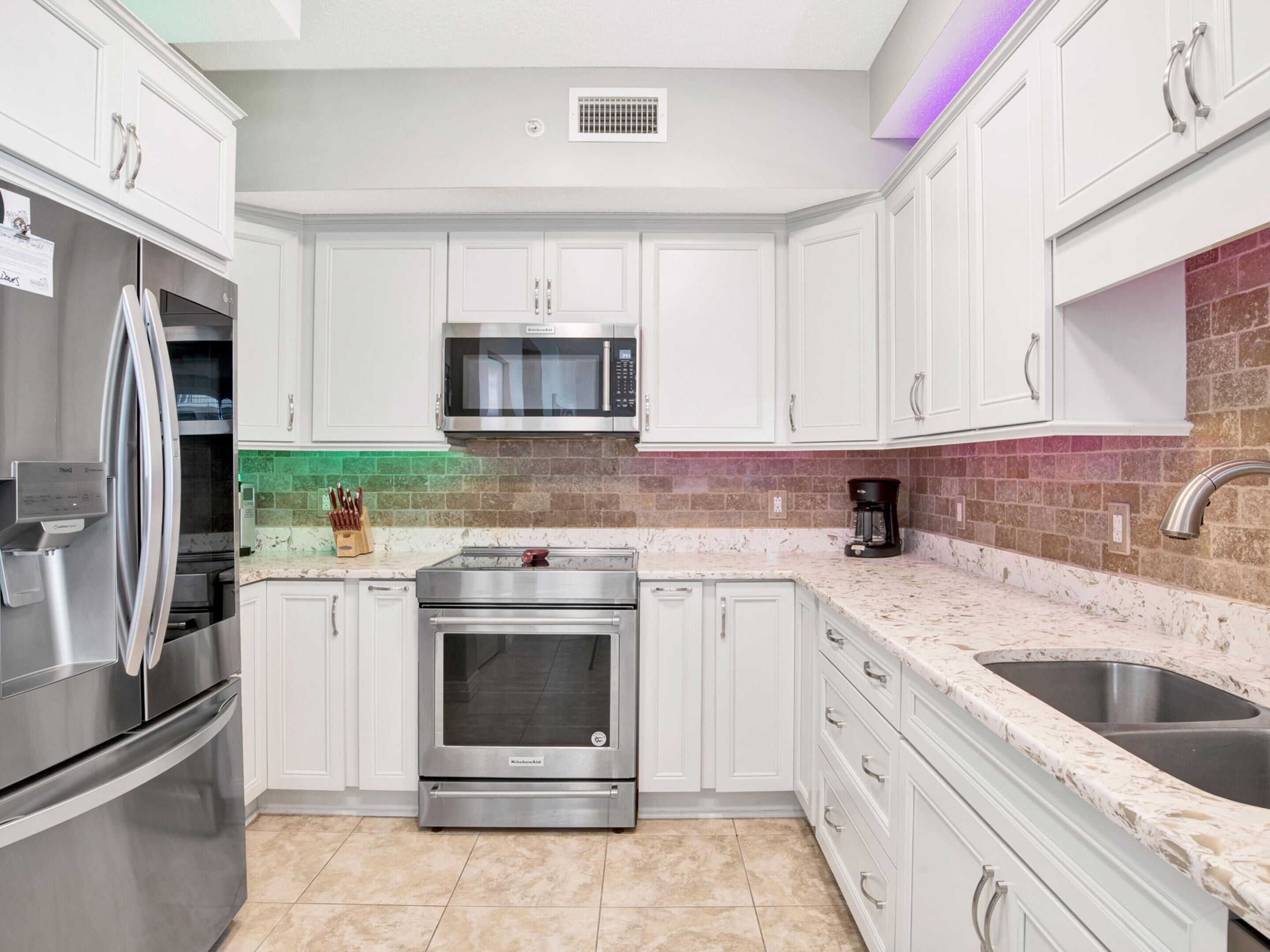 A modern kitchen with white cabinets, stainless steel appliances, a microwave, and a double sink.