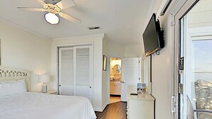 A hotel room with a bed, a ceiling fan, a TV, and a view of the kitchen and bathroom. - Baywatch by Southern Vacation Rentals (Pensacola Beach)