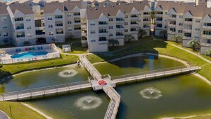 A multi-story hotel with balconies, a swimming pool, and a water feature with fountains. - Baywatch by Southern Vacation Rentals (Pensacola Beach)