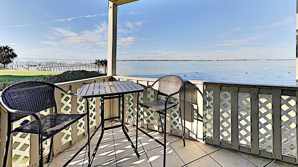 A covered outdoor seating area with a view of the water and a distant pier. - Baywatch by Southern Vacation Rentals (Pensacola Beach)