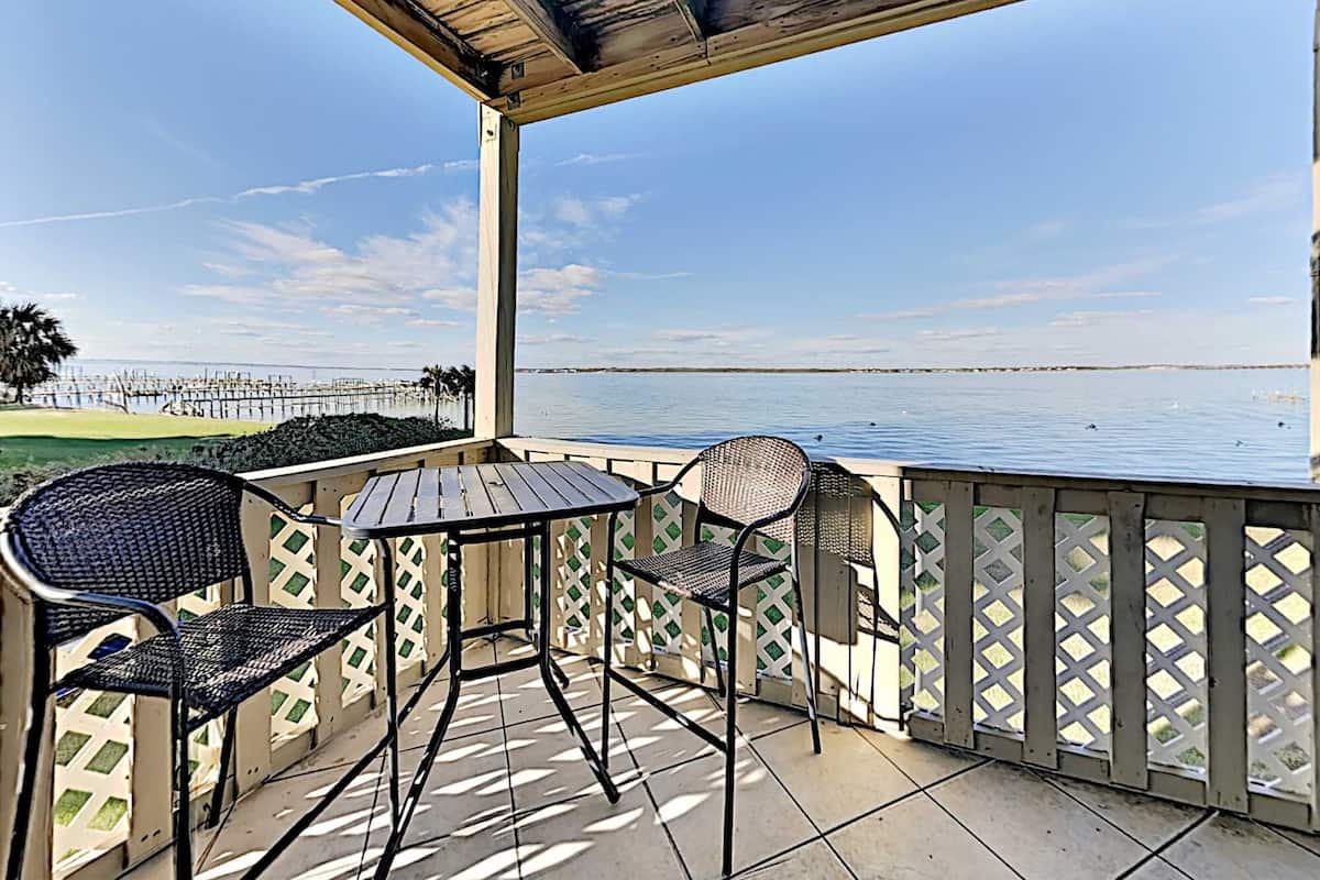 A covered outdoor seating area with a view of the water and a distant pier.