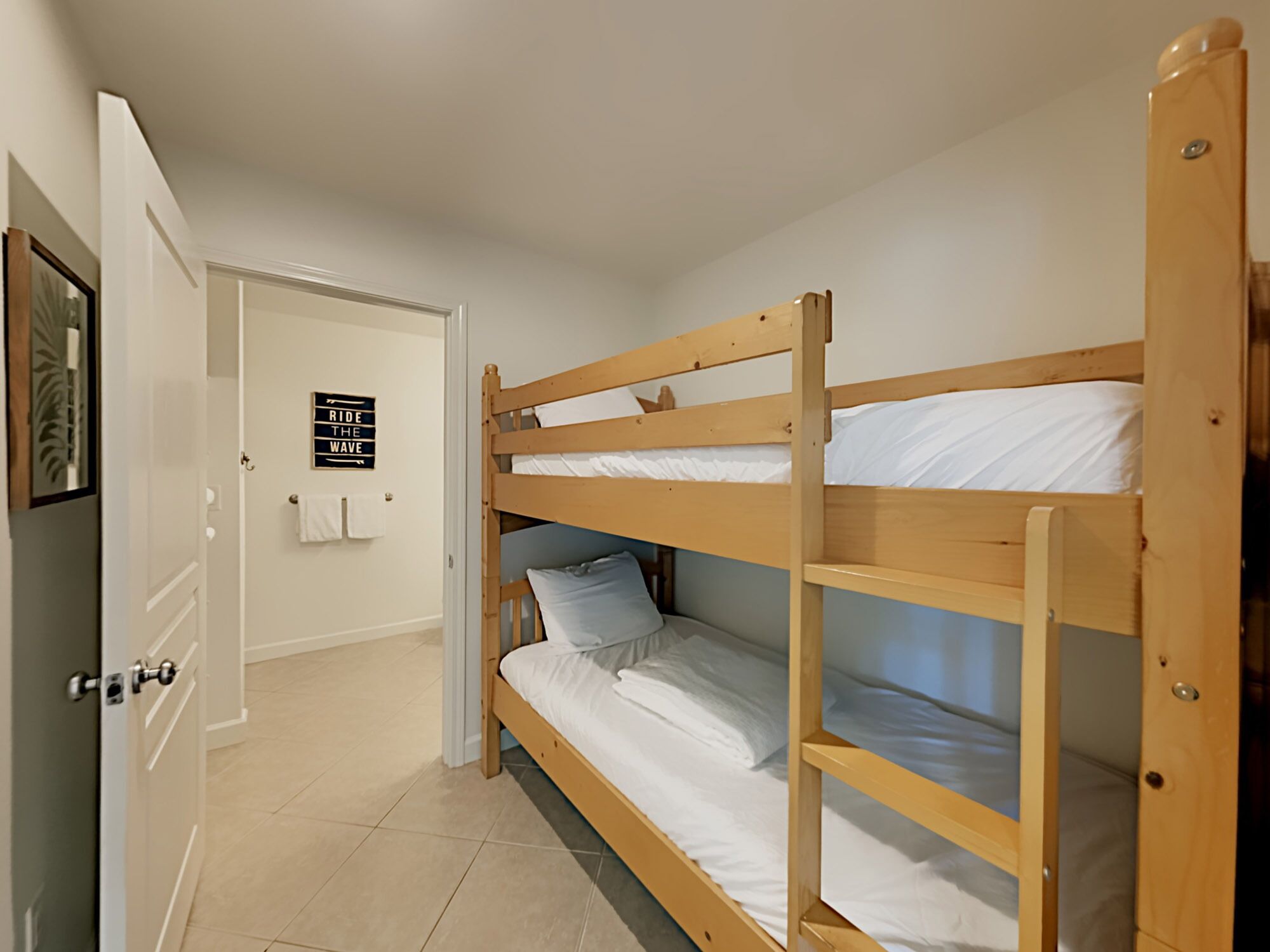 A bunk bed room with a door leading to a bathroom. A sign on the wall reads "Ride the Wave".