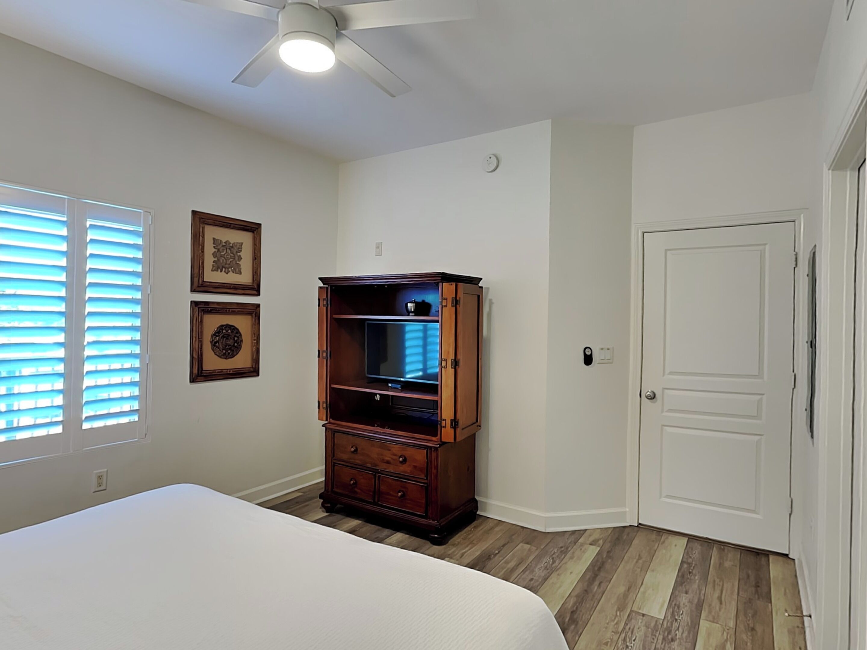 A bedroom with a bed, a wooden cabinet, a ceiling fan, and a door.