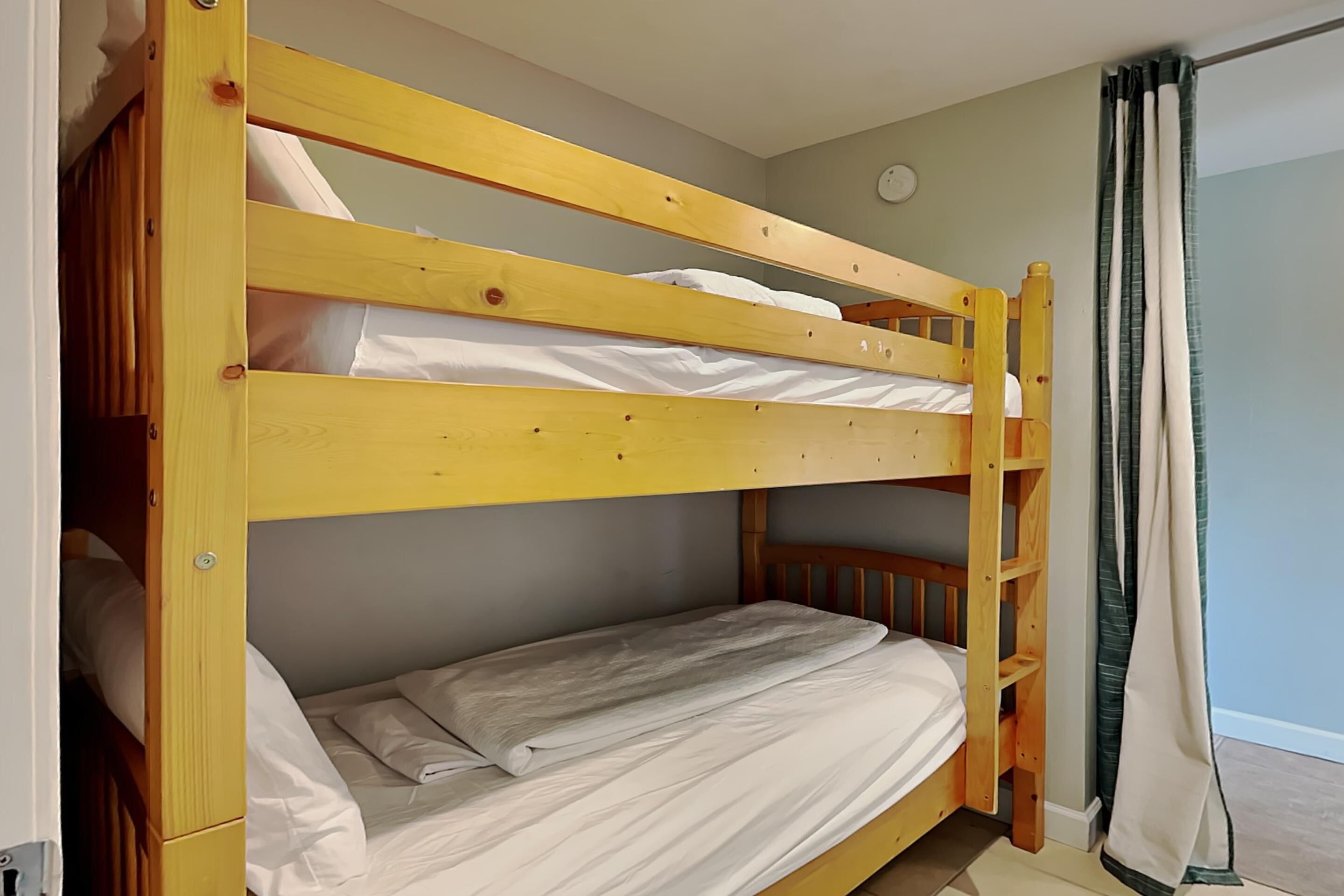 Uma cama beliche com escada, roupa de cama branca e uma cortina do lado direito.