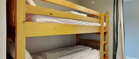 Uma cama beliche com escada, roupa de cama branca e uma cortina do lado direito.
