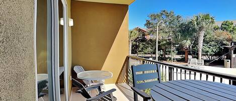 A balcony with a table and chairs, a small round table, and a view of palm trees and buildings.