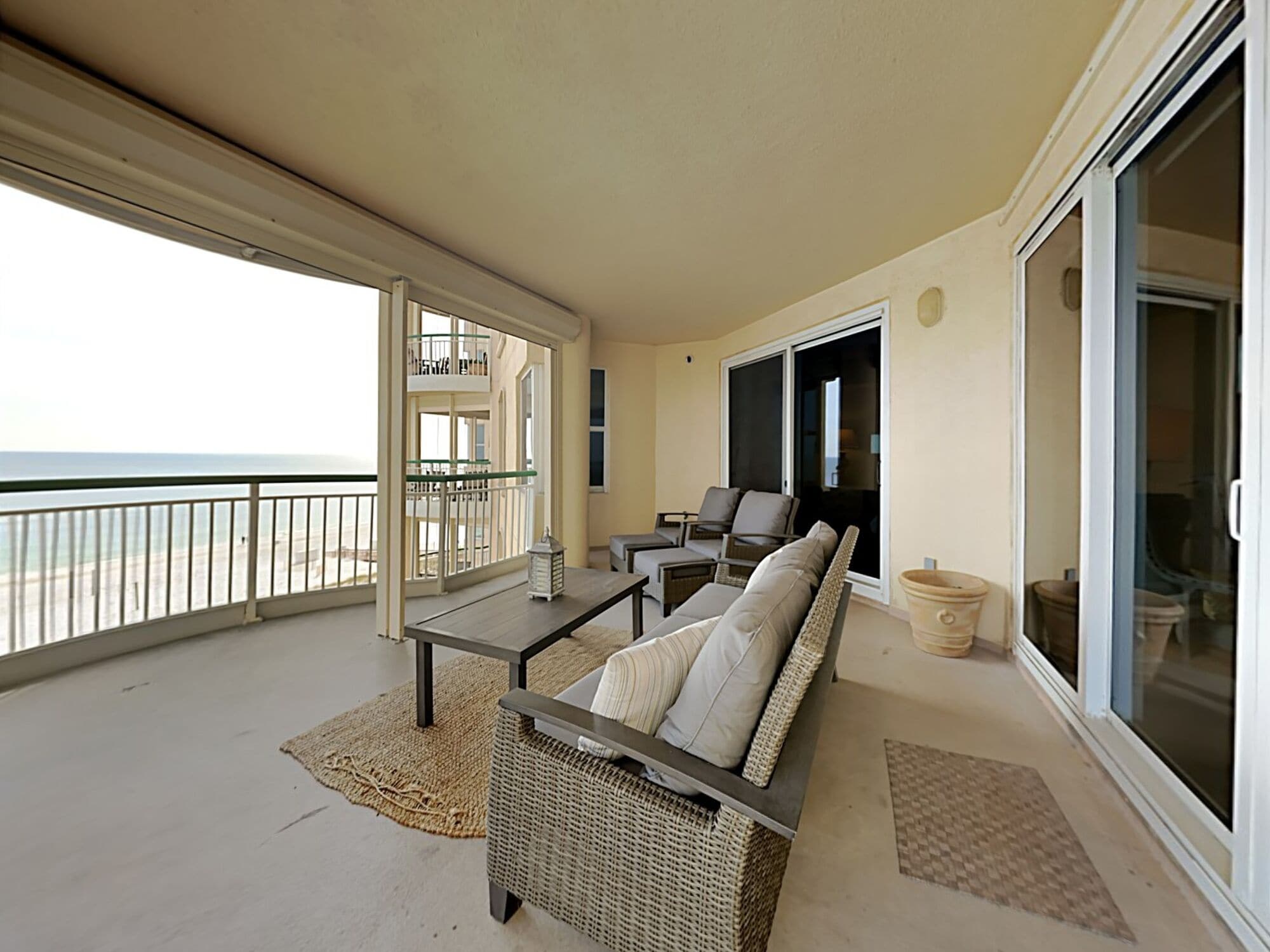 A balcony with a wicker sofa, a small table, and a view of the ocean.