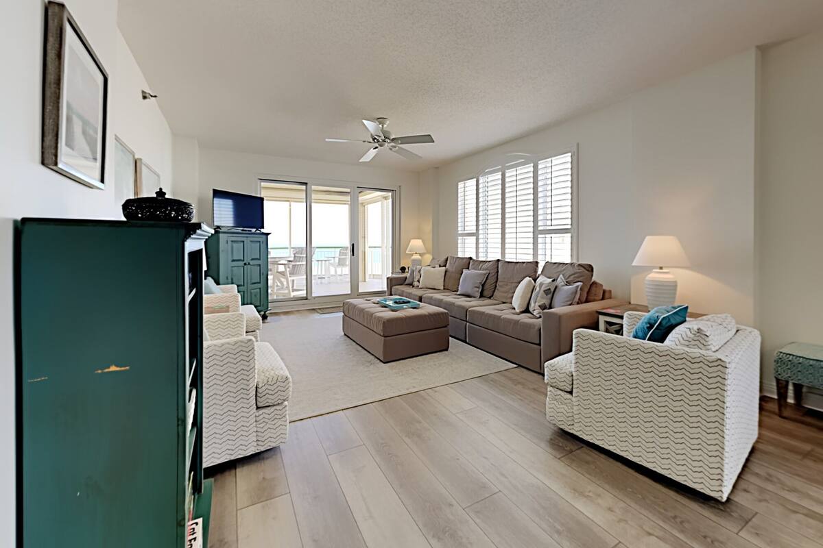 A spacious living room with a large sofa set, a television, and a sliding glass door leading to an outdoor area.