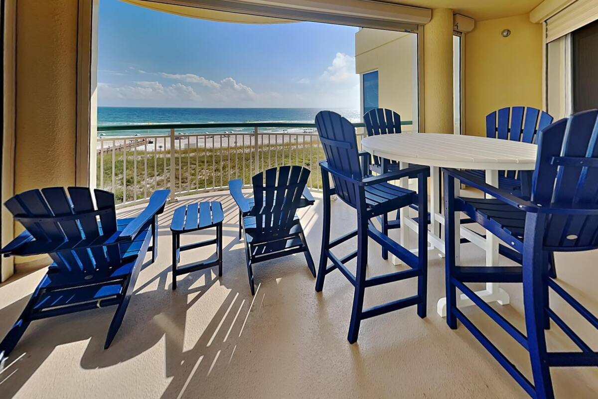 A balcony with a table and chairs, overlooking a beach.