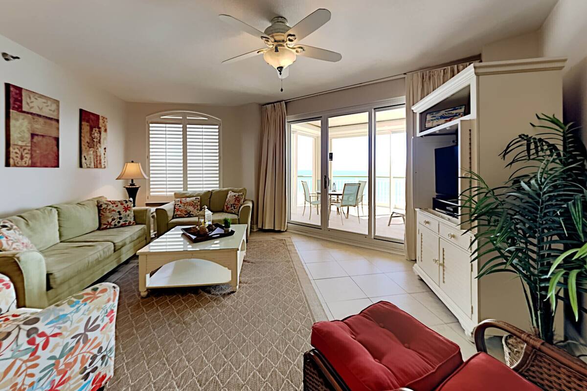 A living room with a ceiling fan, a sofa, a coffee table, a TV, and a sliding glass door leading to an outdoor area.