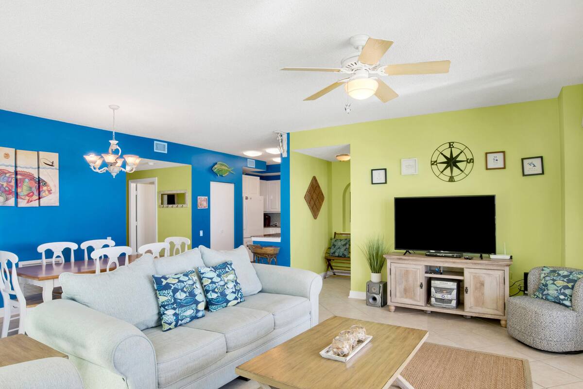 A living room with a sofa, coffee table, TV, and a ceiling fan.