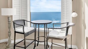A corner room with a view of the ocean, featuring a round table and two wicker chairs with cushions. - Beach Colony Towers by Southern Vacation Rentals (Pensacola)