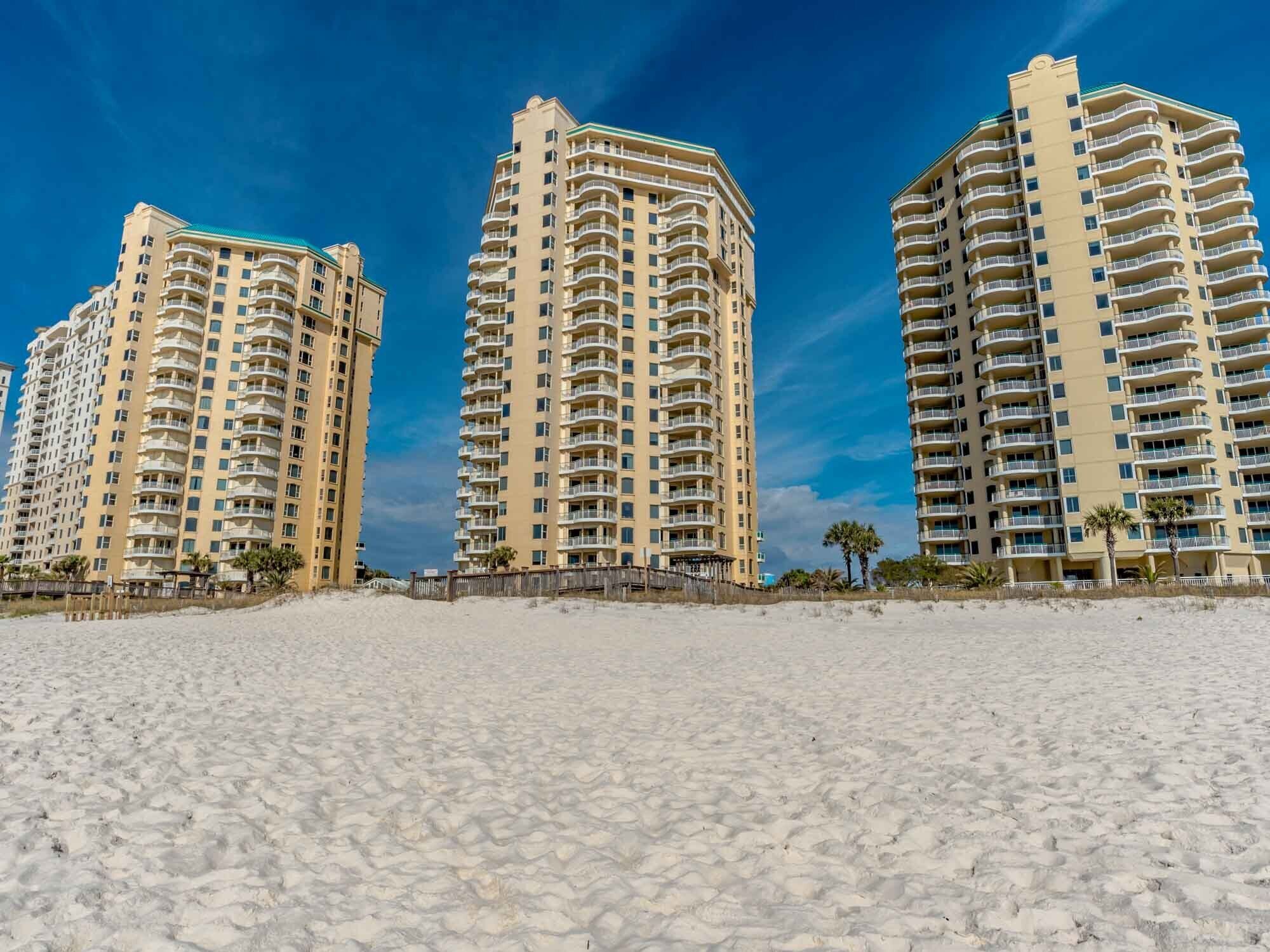 Three high-rise buildings with balconies, located on a sandy beach.