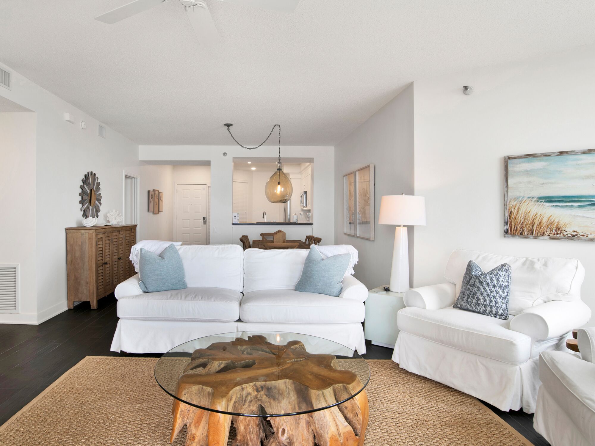 Una sala de estar moderna con una mesa de centro de vidrio, sofás blancos y un mueble de madera.