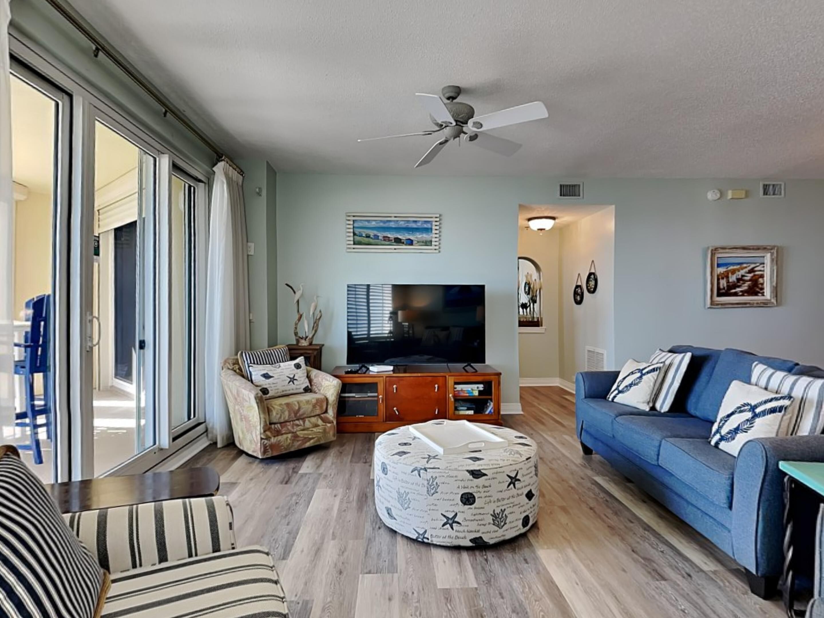 A living room with a television, sofa, ottoman, and a ceiling fan.