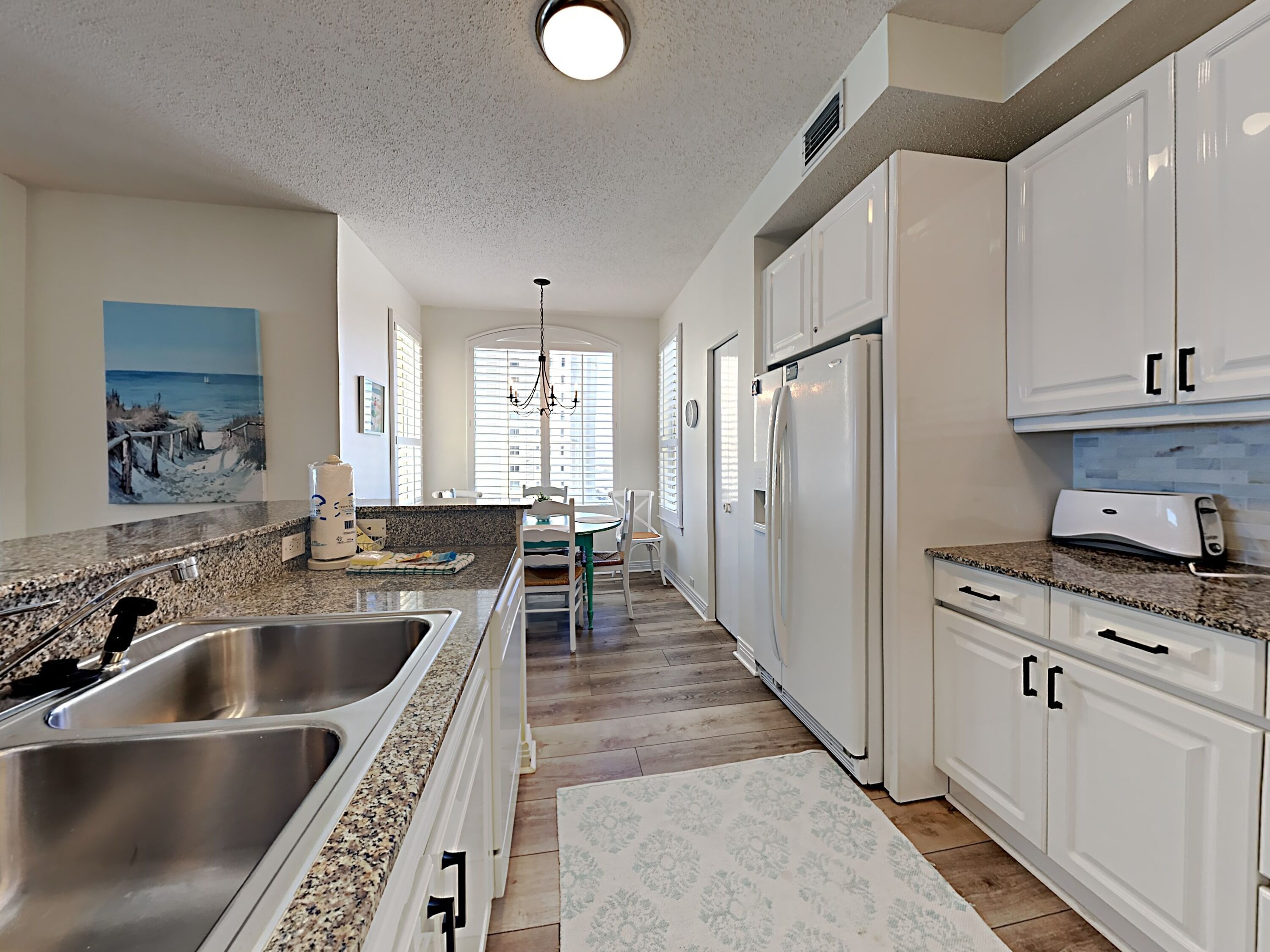 A kitchen with white cabinets, granite countertops, stainless steel sinks, and a refrigerator.