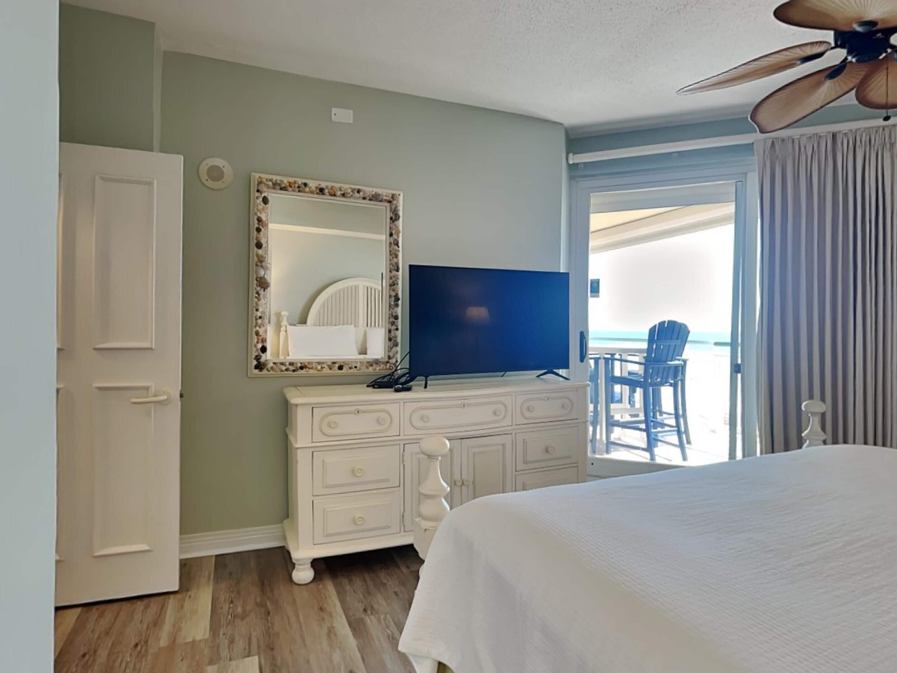 A hotel room with a bed, a television, a dresser, a mirror, and a balcony with a chair.