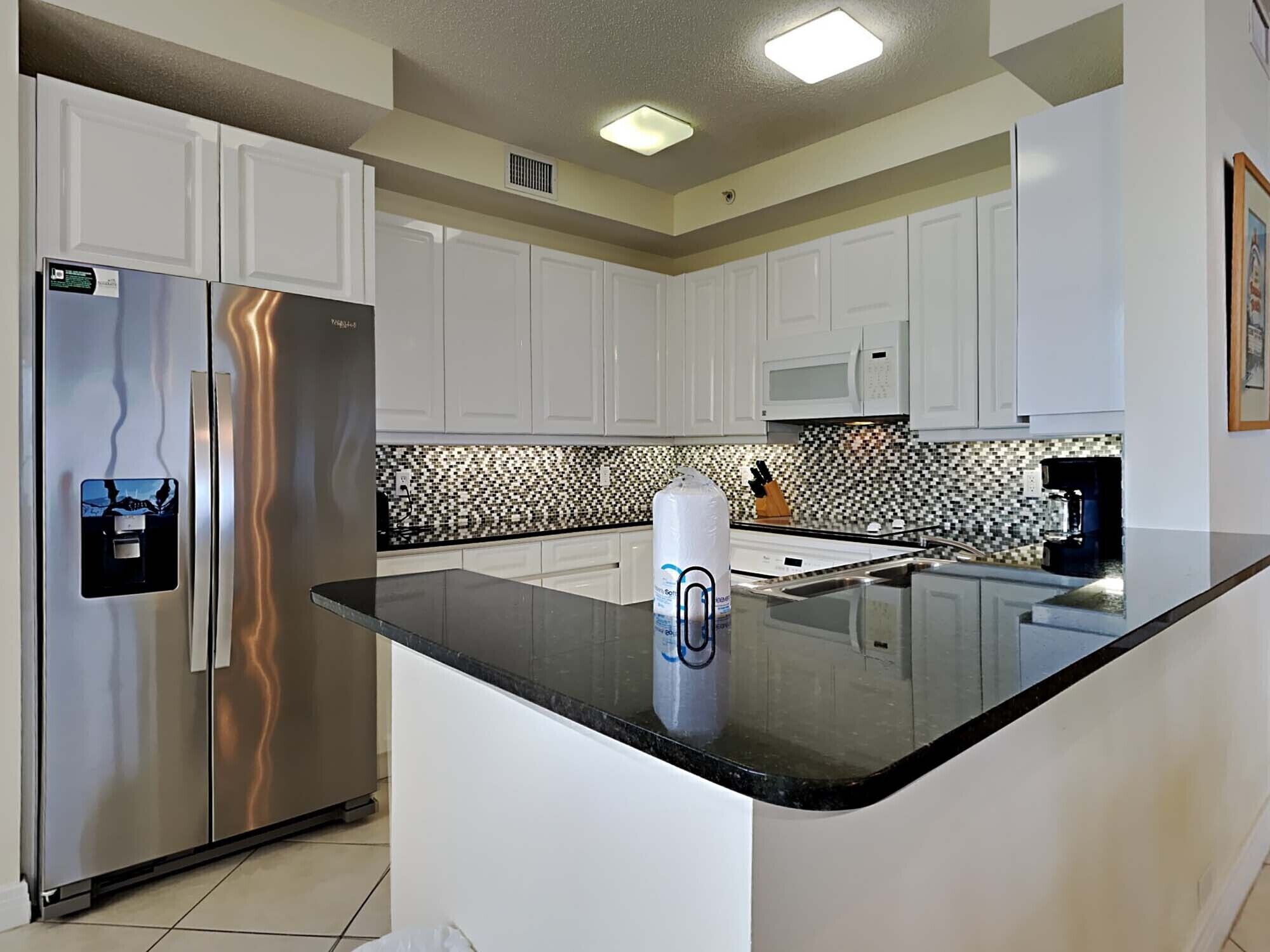 A modern kitchen with white cabinets, stainless steel appliances, a black countertop, and a patterned backsplash.