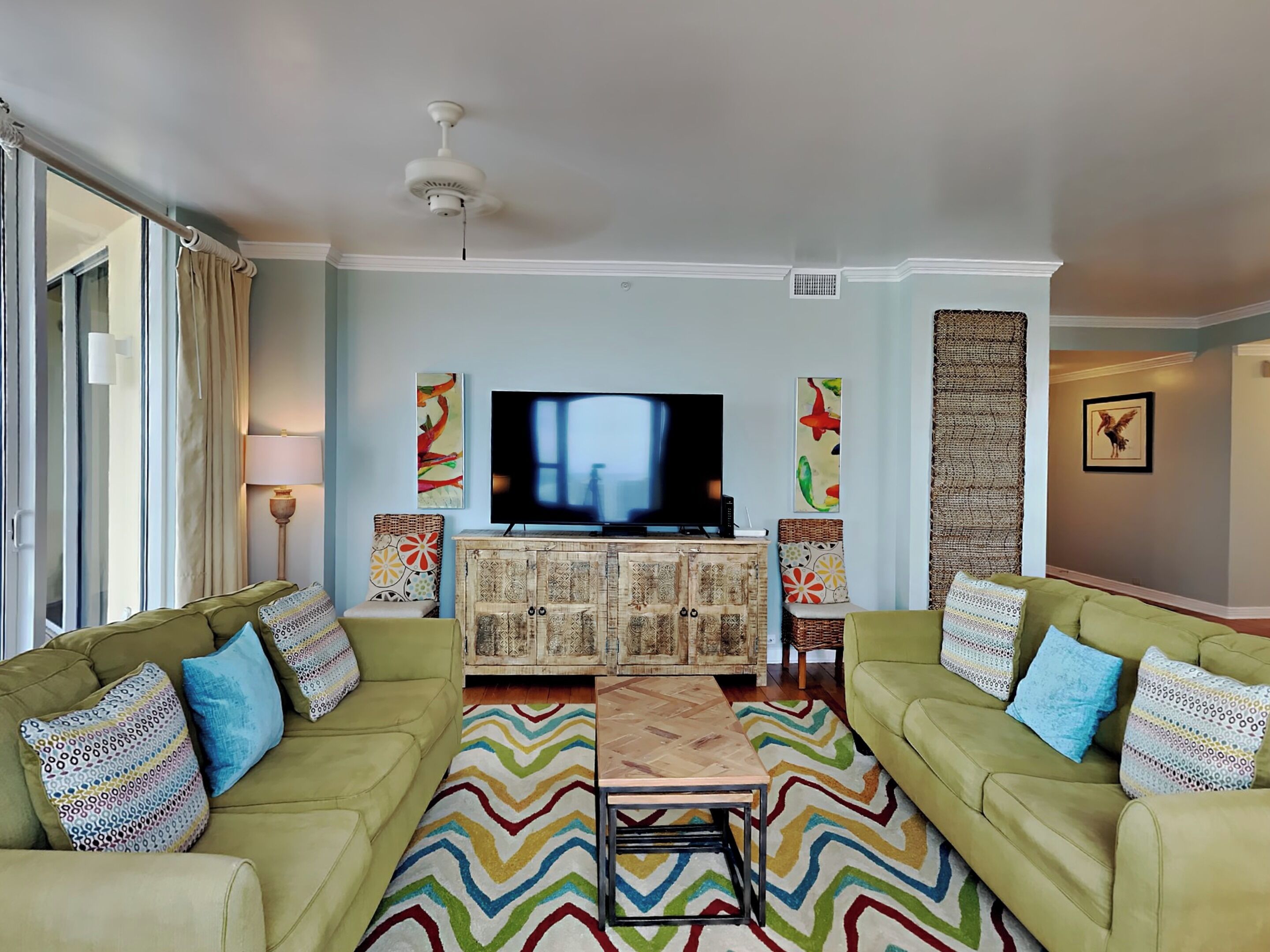 A living room with two green sofas, a coffee table, a TV, and decorative wall art.