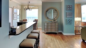 A modern kitchen with a bar area, a dining set, and a large window offering a city view. - Beach Colony East by Southern Vacation Rentals (Pensacola)