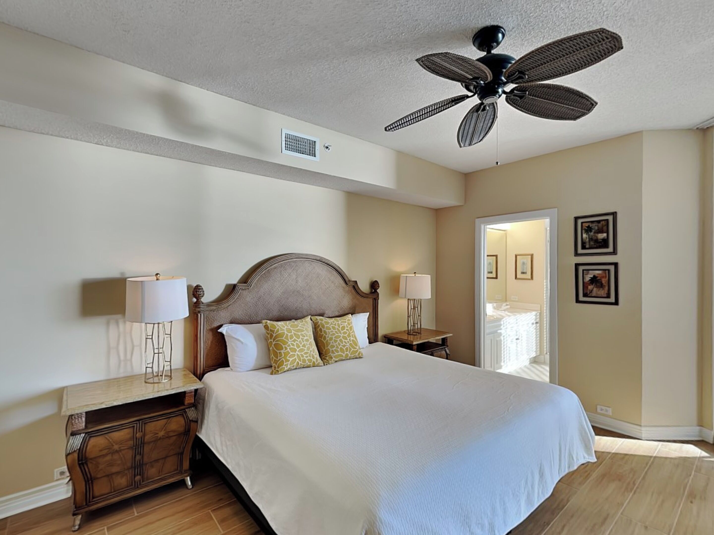 Habitación de hotel con una cama grande, un ventilador de techo, una mesita de noche y un aparador.