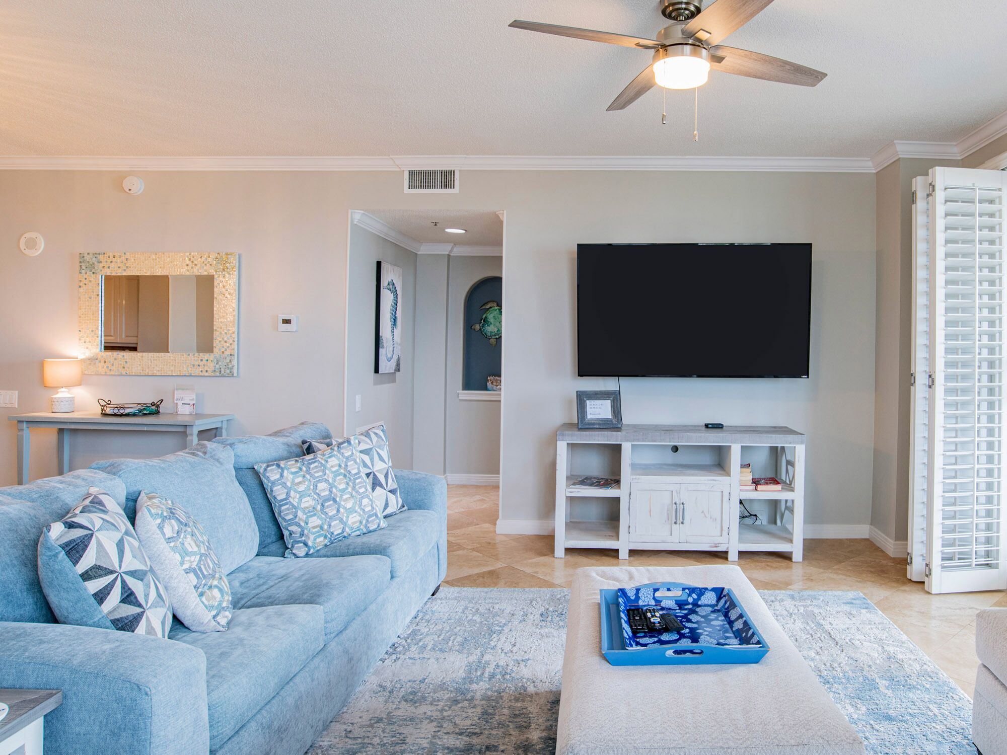 A living room with a blue sofa, a flat-screen TV, a ceiling fan, and a white cabinet.