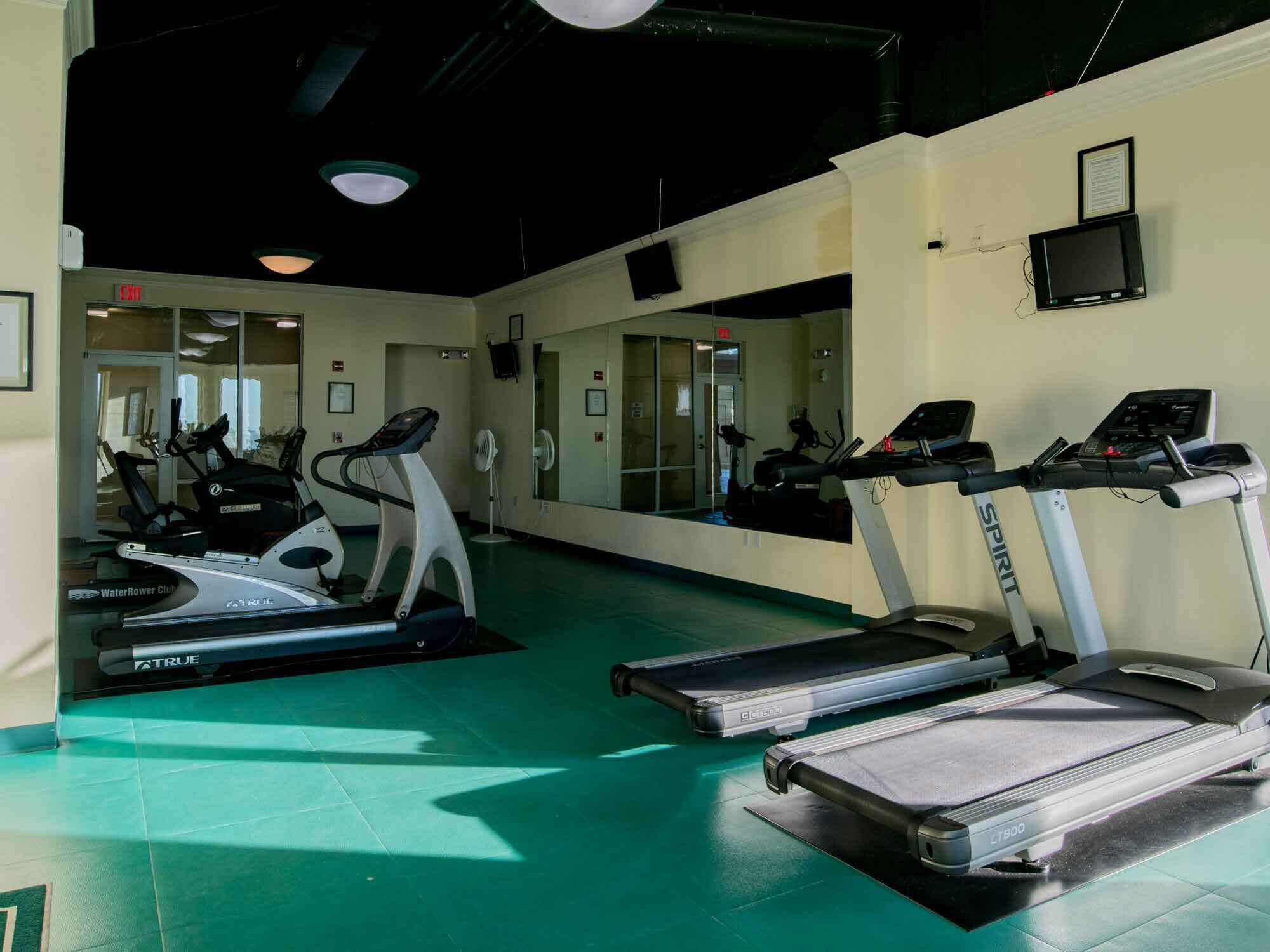 A gym with treadmills, ellipticals, and a mirrored wall.