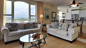 A living room with two sofas, a glass coffee table, and a view of the city through large windows. - Beach Colony East by Southern Vacation Rentals (Pensacola)