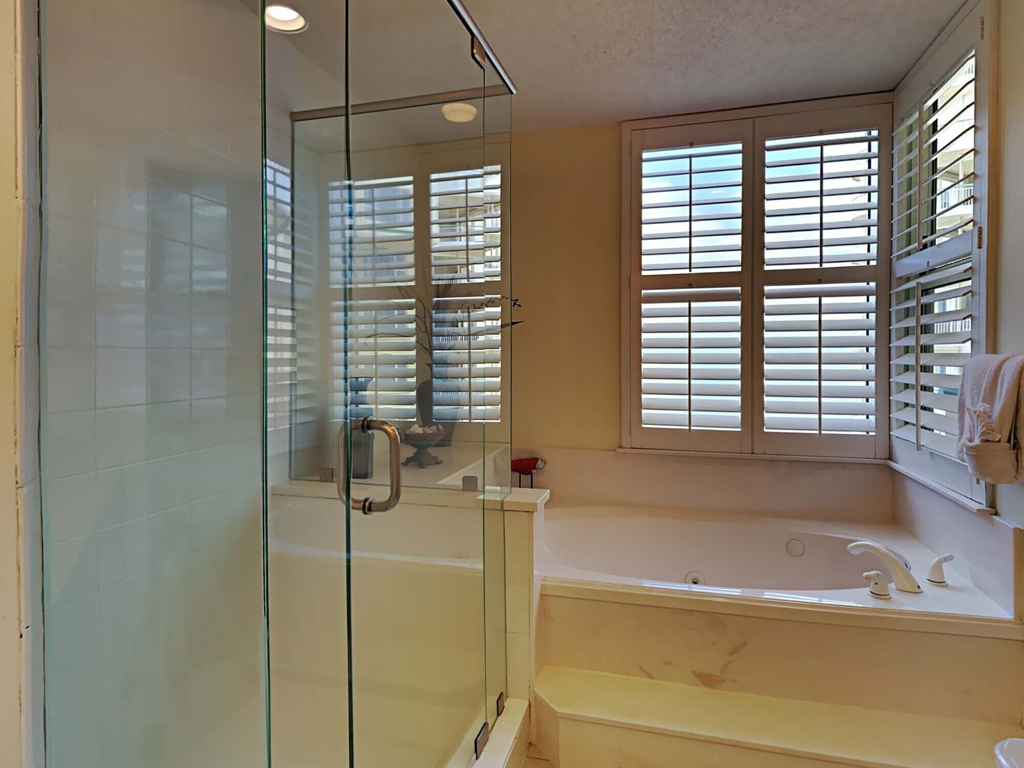 Ein Badezimmer mit Duschkabine aus Glas, einer Badewanne und einem Fenster mit Jalousien.