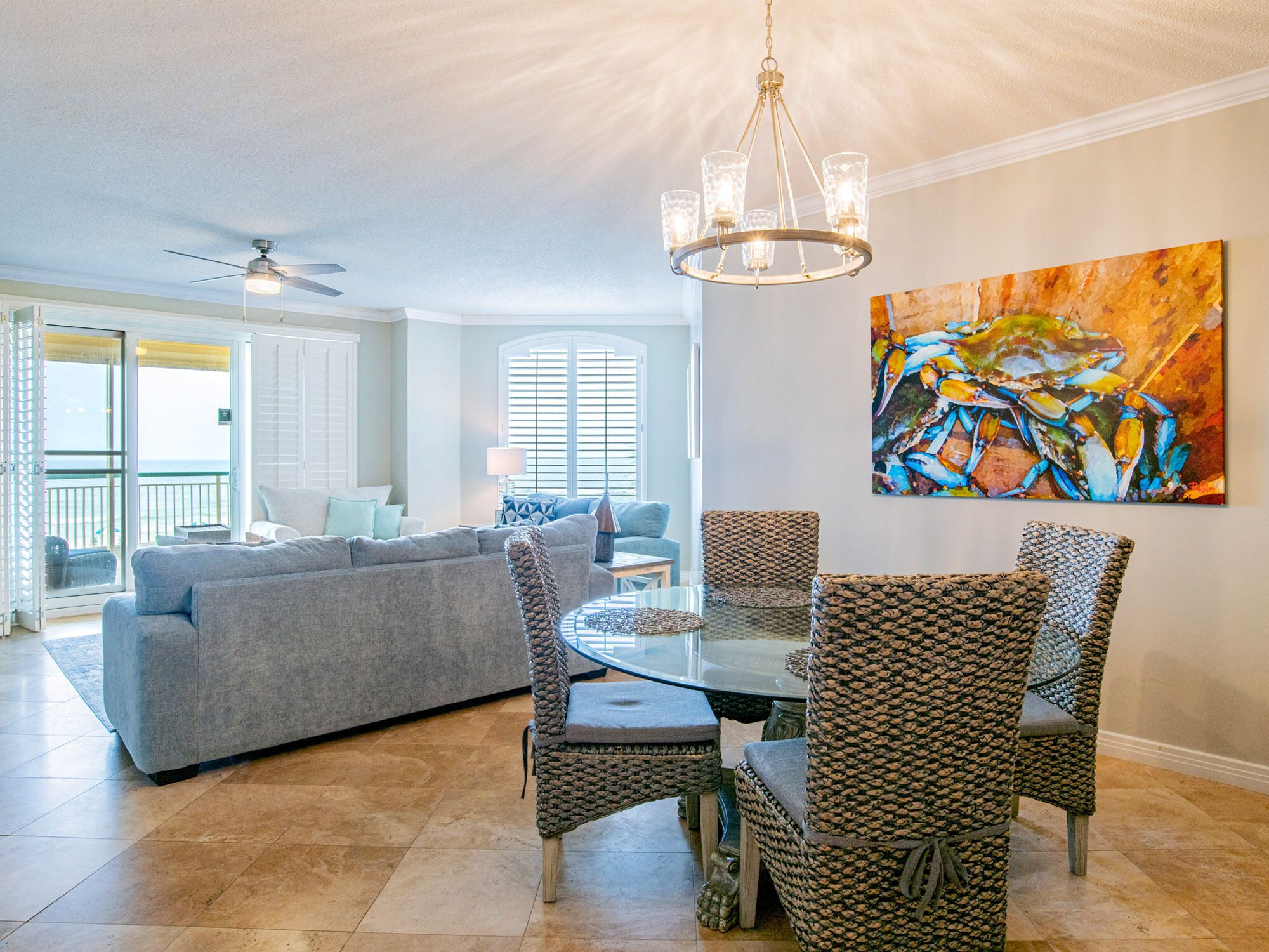 A spacious living area with a gray sofa, wicker chairs, a glass dining table, and a ceiling fan.