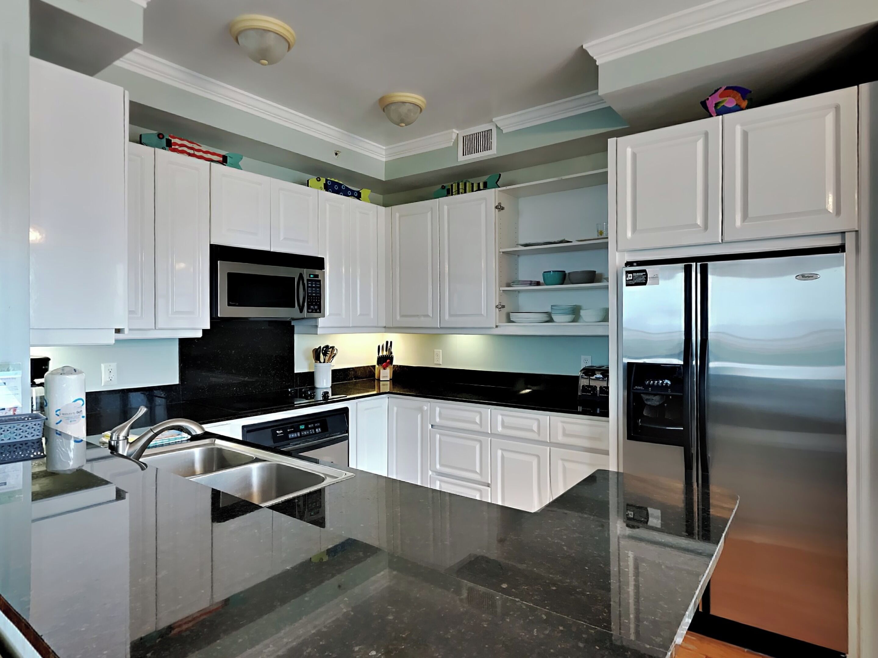 A modern kitchen with white cabinets, a stainless steel refrigerator, a microwave, and a black countertop.