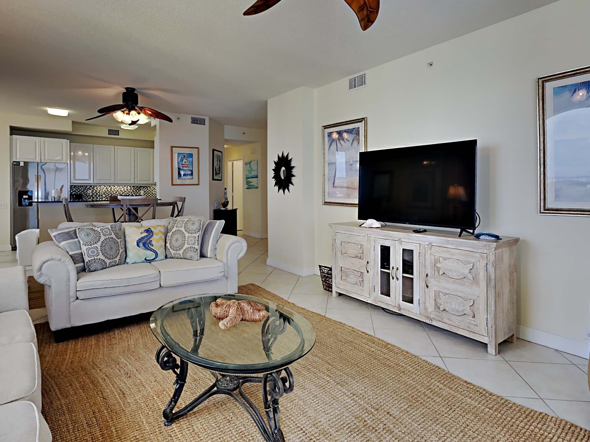 A living room with a sofa, coffee table, TV, and a kitchen in the background.