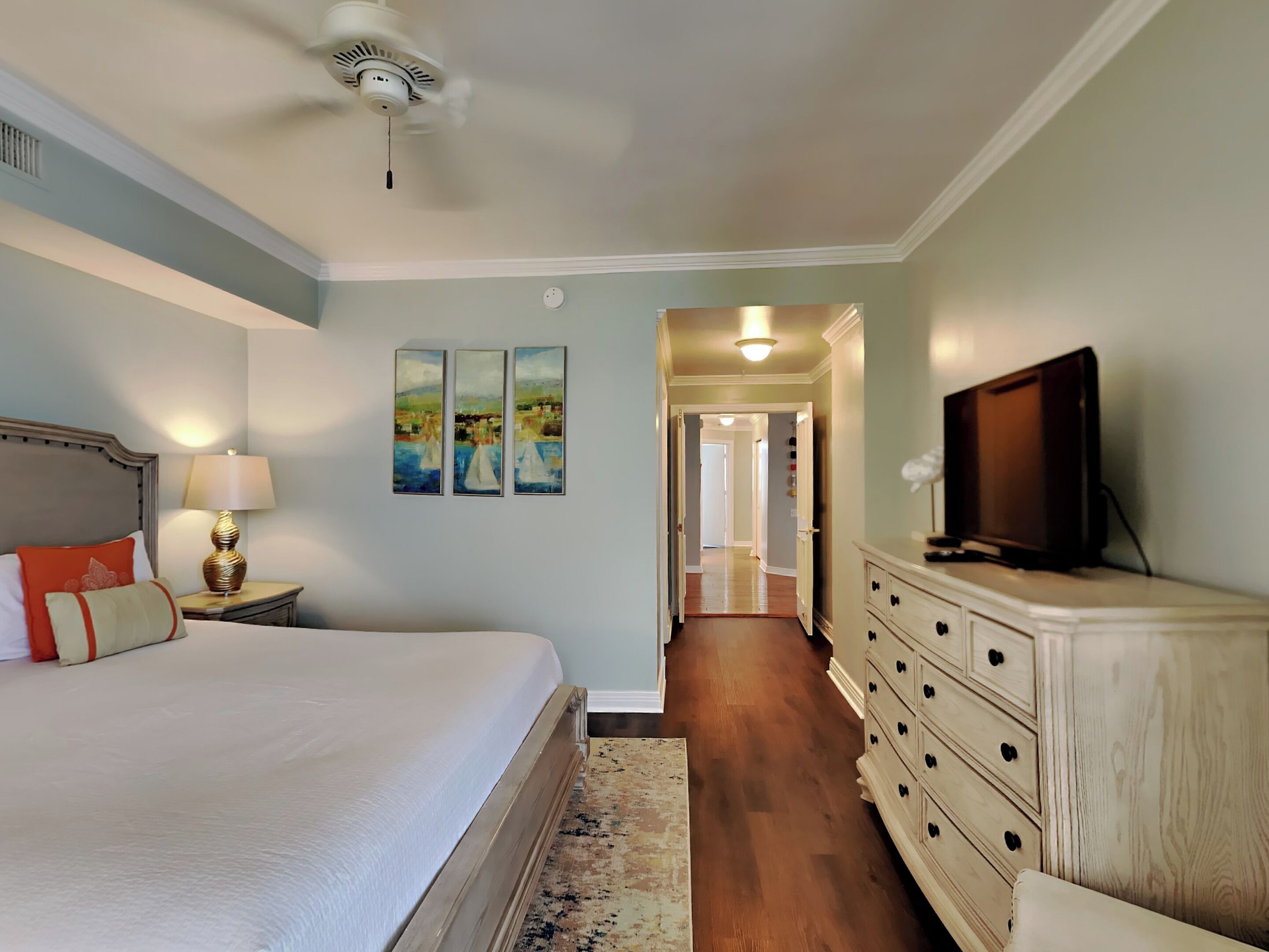 A hotel room with a bed, a dresser, a television, and a hallway leading to another room.