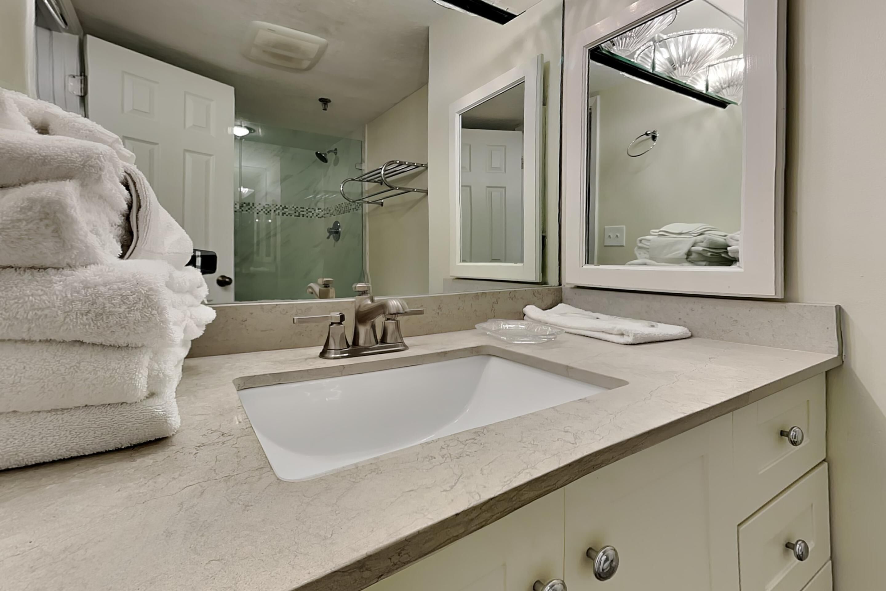 A bathroom with a sink, mirror, and stacked towels.