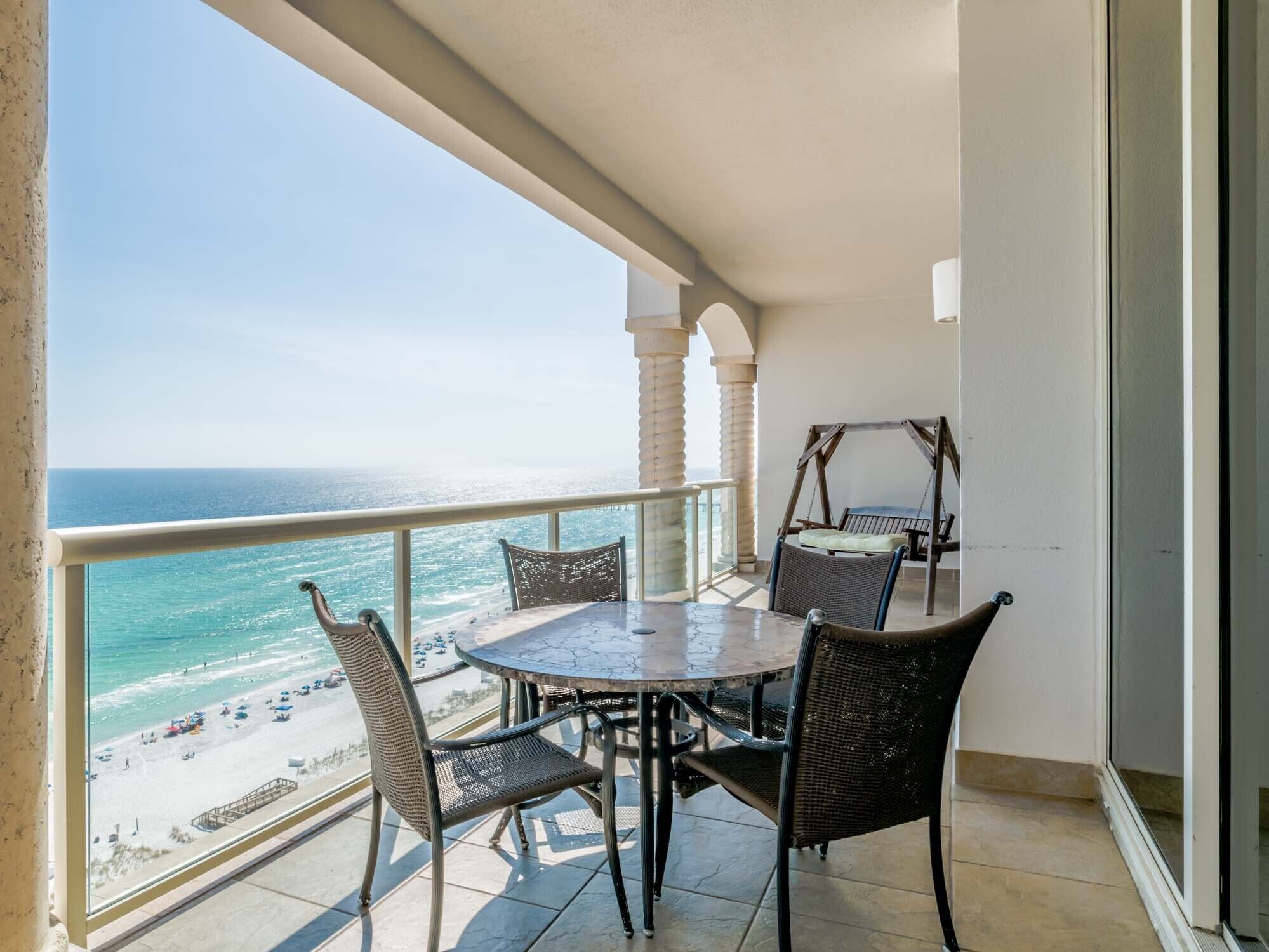 A balcony with a table and chairs, overlooking a beach and the ocean.