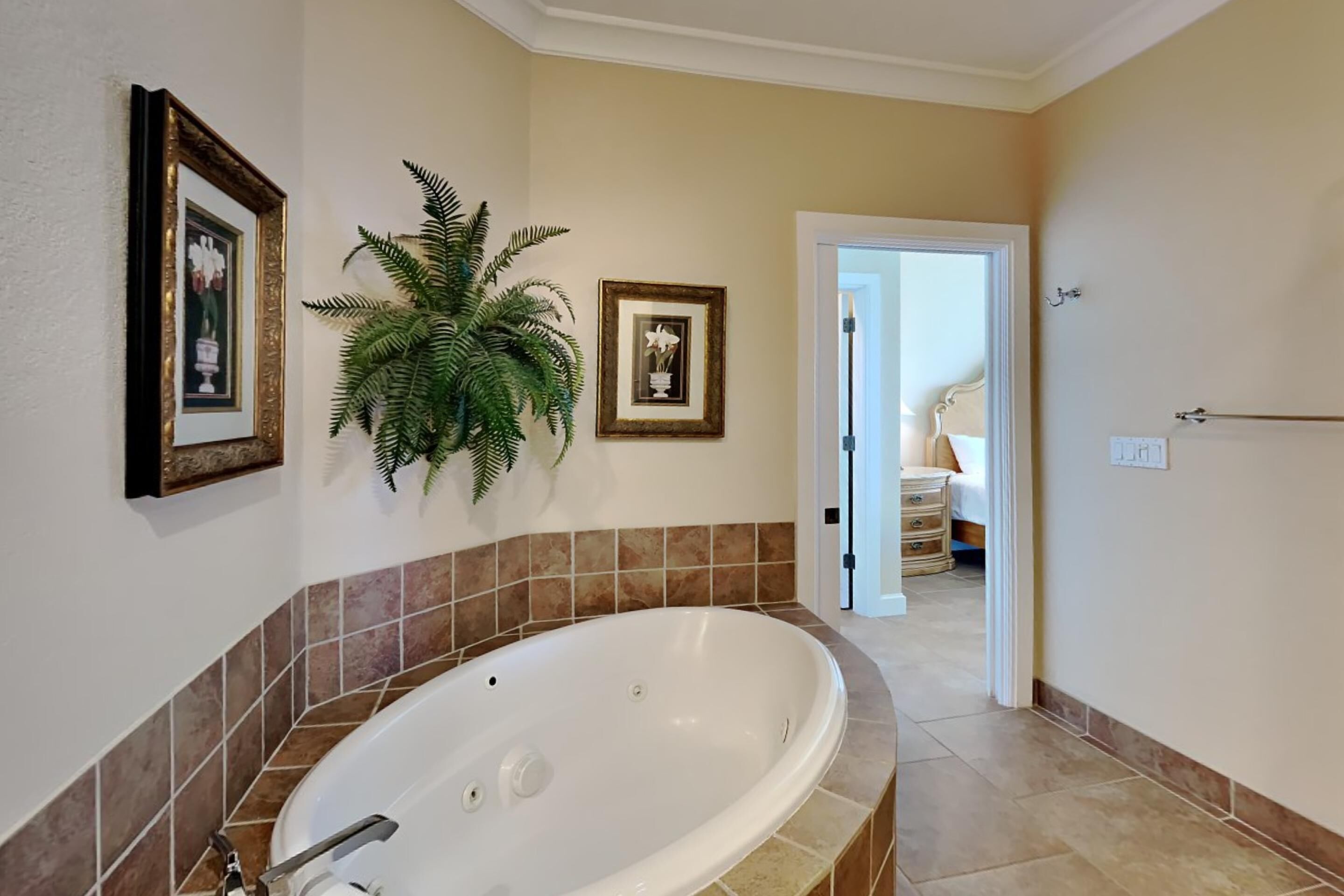 Un baño con una bañera grande, una planta en maceta y cuadros en la pared.