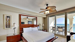 A spacious bedroom with a large bed, a ceiling fan, a balcony with outdoor seating, and a view of the ocean. - Beach Club by Southern Vacation Rentals (Pensacola Beach)