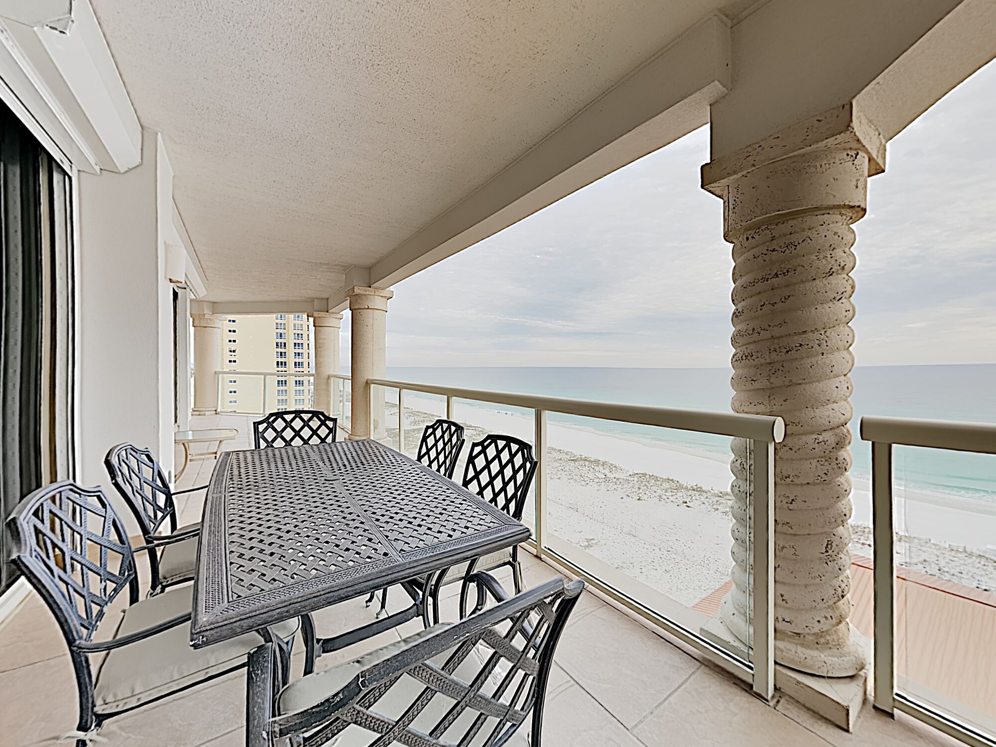 A covered outdoor dining area with a table and chairs, overlooking a beach.