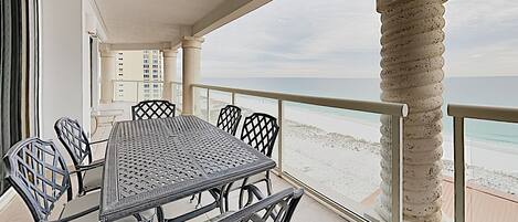A covered outdoor dining area with a table and chairs, overlooking a beach.