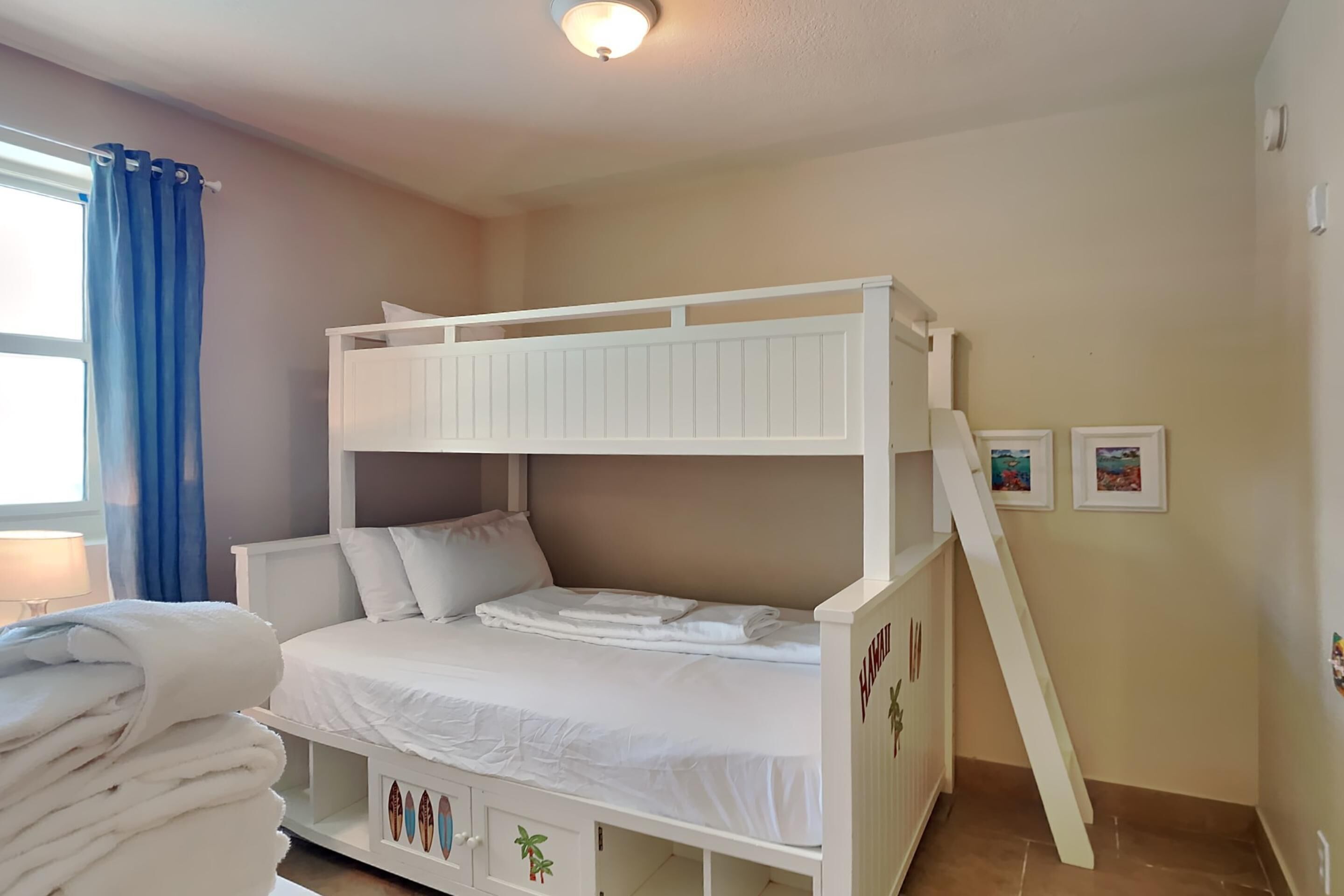 Een slaapkamer met een stapelbed, een wit hoofdbord, een ladder en een stapel witte handdoeken.