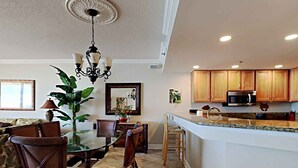 Una cocina moderna con armarios de madera, una isla central y una zona de comedor con mesa y sillas de vidrio.