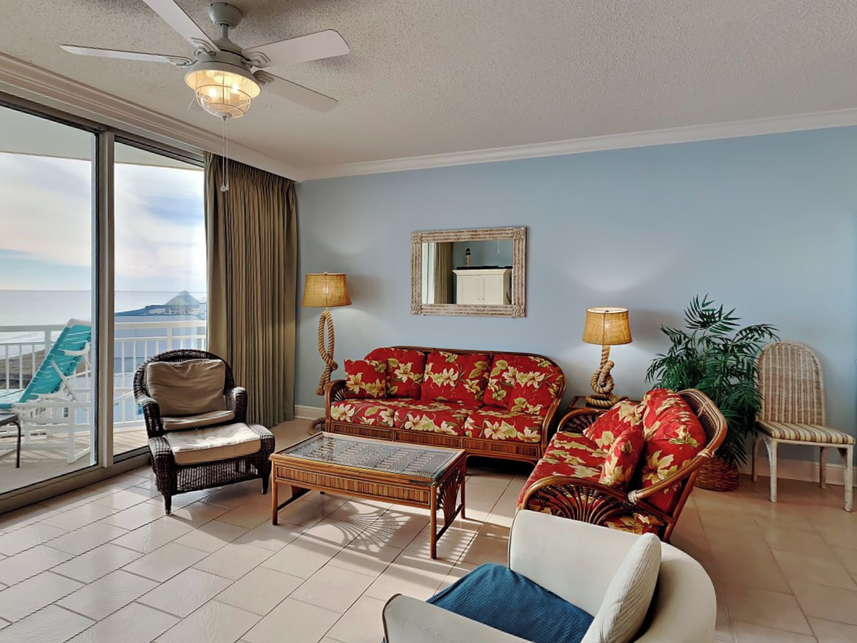 A spacious living room with a large window, a ceiling fan, a sofa, a chair, a small table, and a potted plant.
