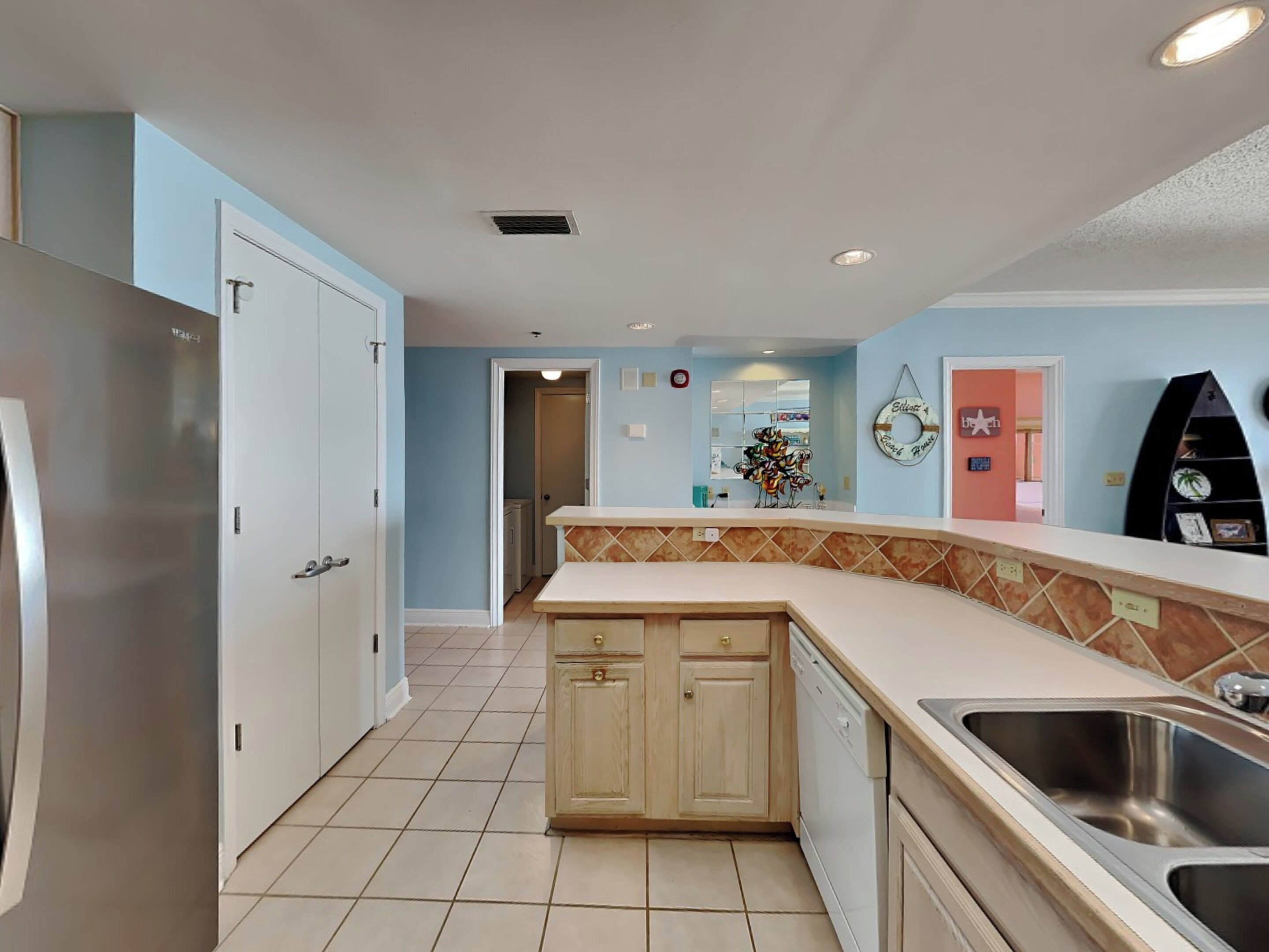 A kitchen with a refrigerator, sink, and cabinets. There is a door leading to another room.