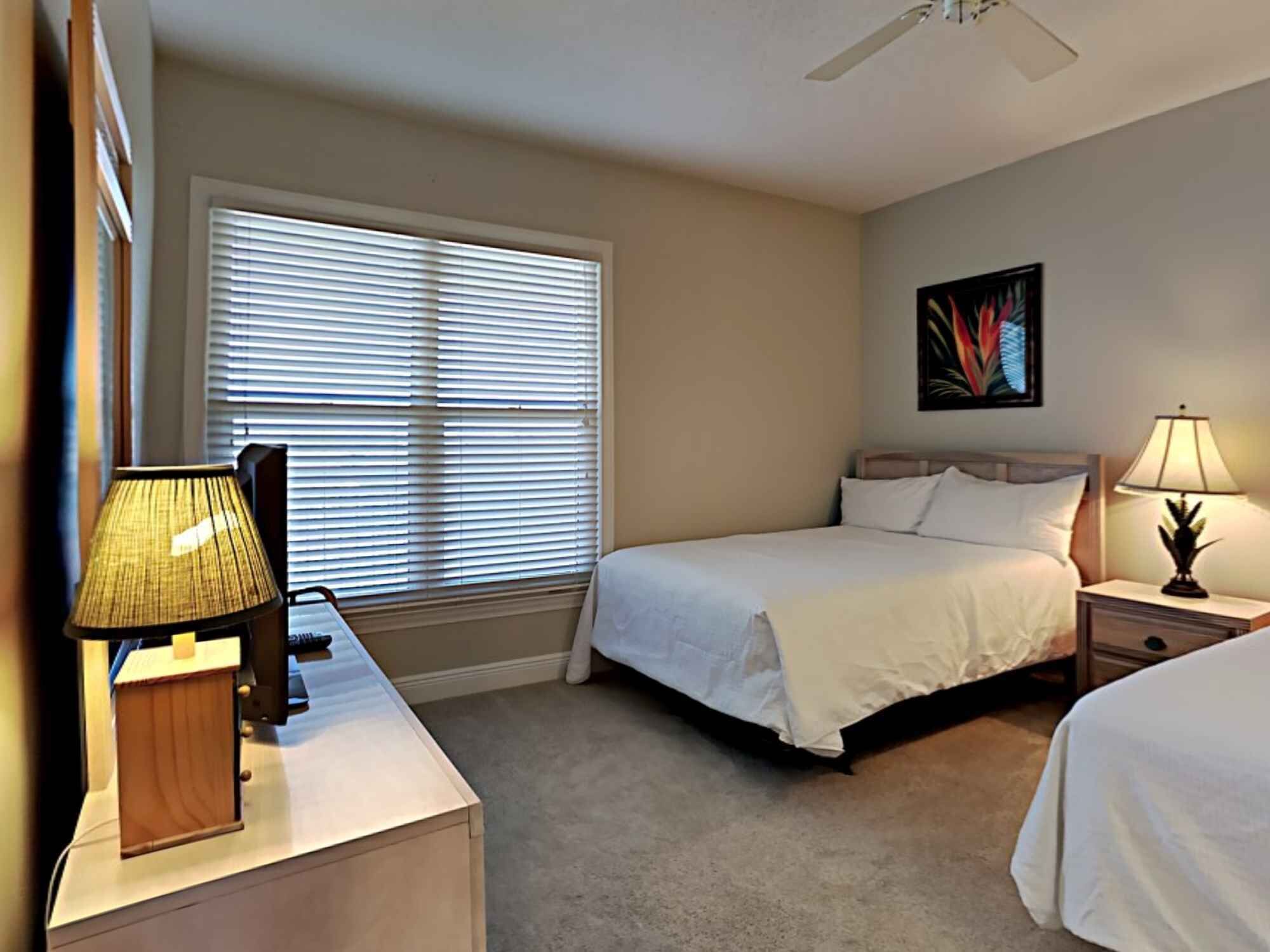 A bedroom with a bed, bedside table, lamp, and a window with blinds.