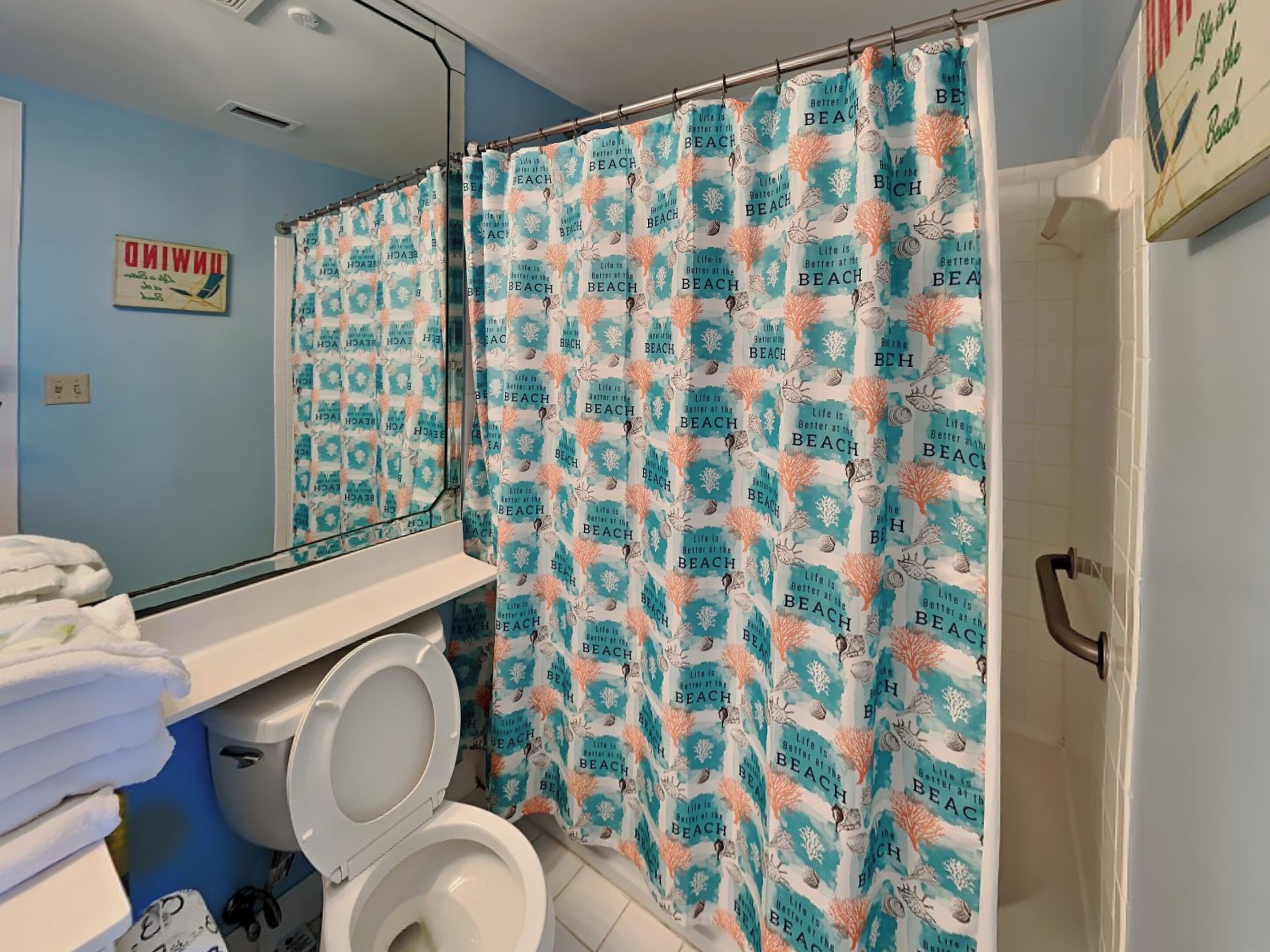 A bathroom with a shower curtain featuring a beach theme, a toilet, and a sink with towels.